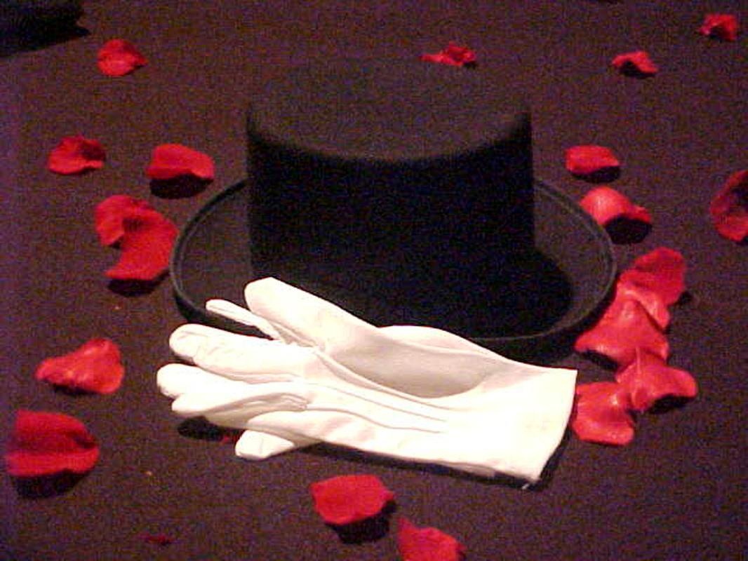 Black top hat with white gloves and rose petals