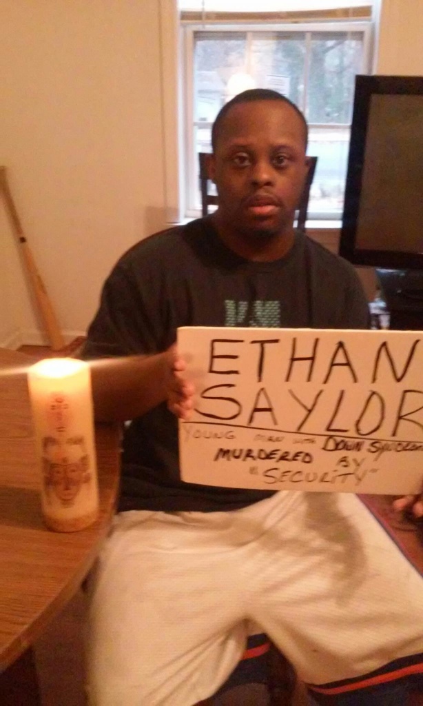 "Dude" holding sign that says Ethan Saylor beside a lit candle